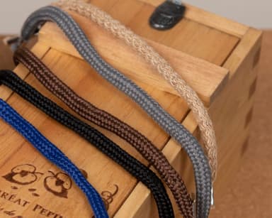 Five braided rope handles - blue, black, brown, grey and natural jute - laid across an engraved pine wine box by Quintessential Canada Inc.